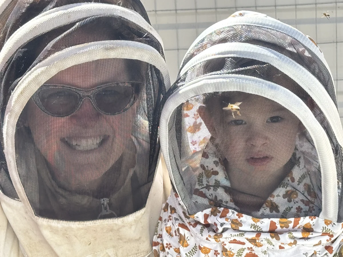 Maggie and Ellie in beekeeping veils at the apiary, with a honeybee resting on Ellie's veil